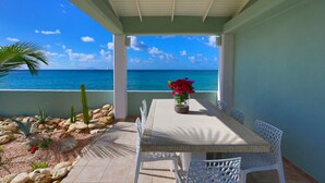 A covered outdoor dining area with a view of the ocean, featuring a table with chairs, a potted plant, and a rock garden. - Beach secrets (Simpson Bay)