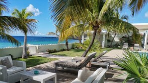 A tropical outdoor lounge area with wicker furniture, a pool, and palm trees. - Beach secrets (Simpson Bay)