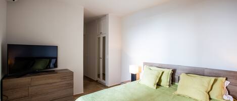 Quarto de hotel com cama, televisão em penteadeira, ventilador de teto e porta para o banheiro.