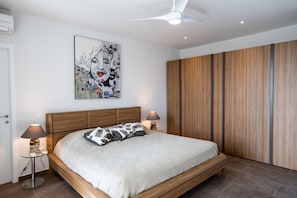 Une chambre moderne avec un cadre de lit en bois, une grande œuvre d’art murale et un ventilateur de plafond.