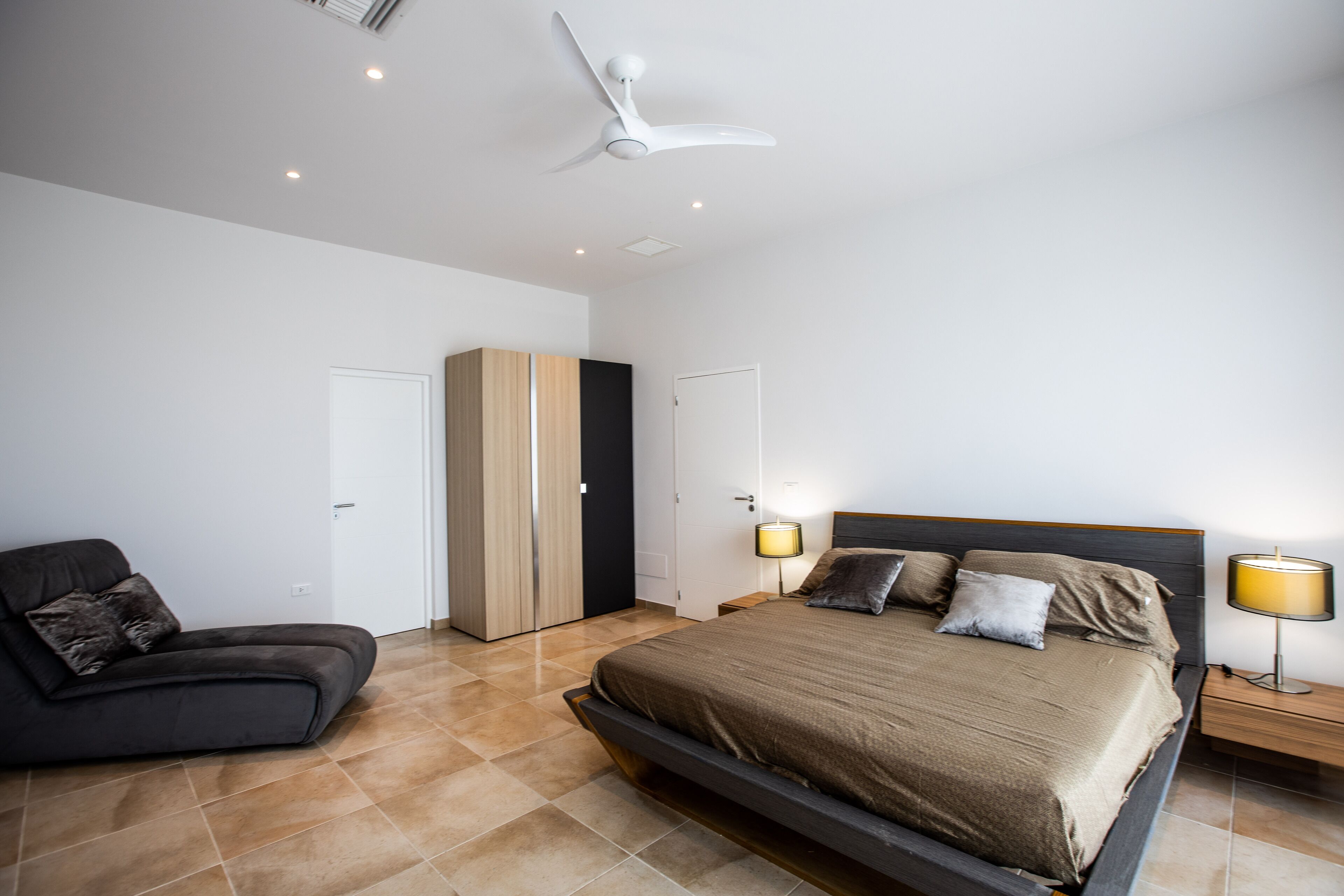 Une chambre à coucher moderne, comprenant un lit, des tables de chevet, une armoire, une chaise et un ventilateur de plafond.