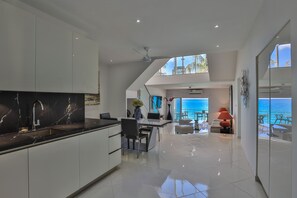 A modern kitchen with a black marble countertop, white cabinets, and a dining area with a view of the ocean. - Cupecoy Beach Club (Lowlands)