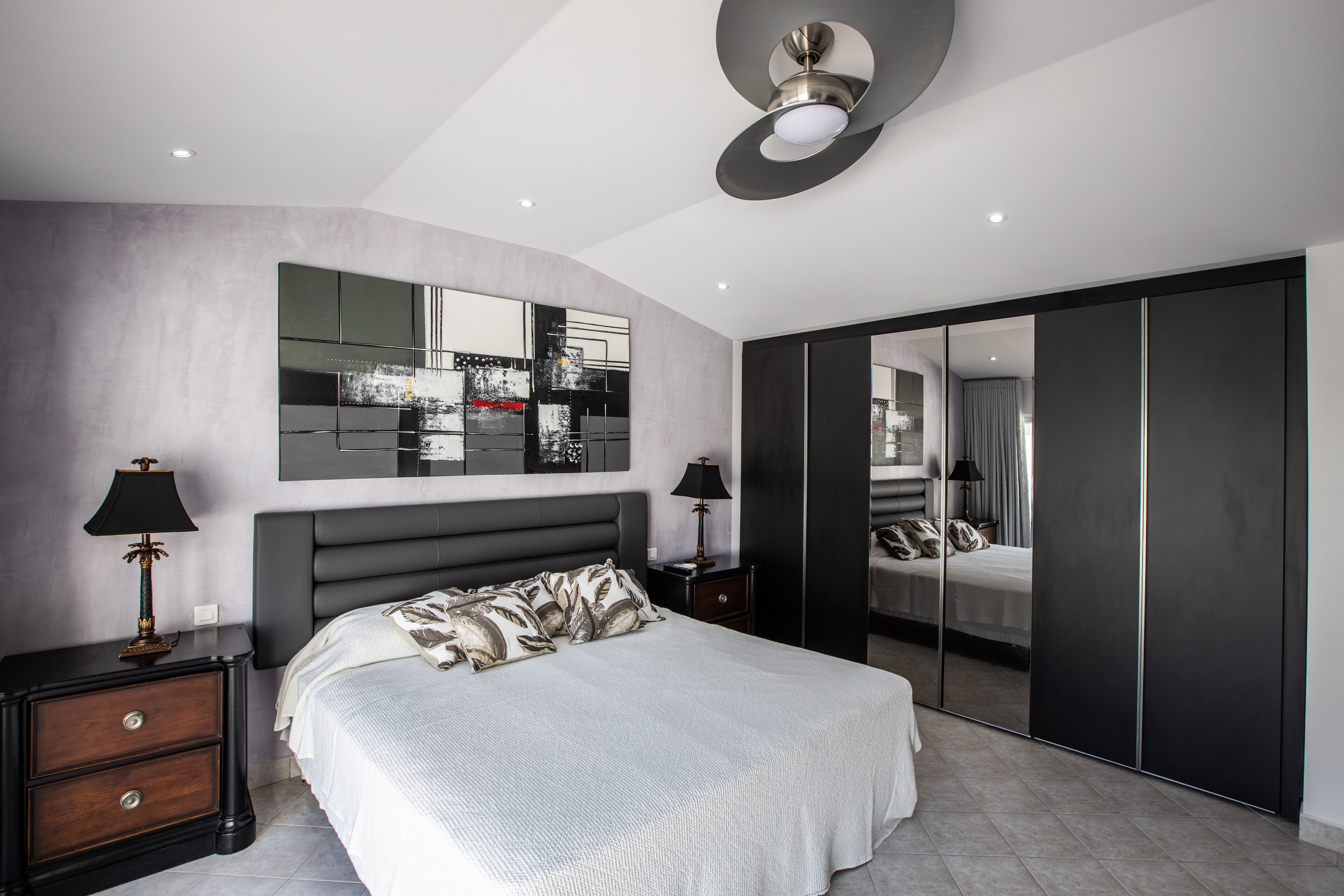 A modern bedroom with a large bed, a wardrobe, and a mirror.