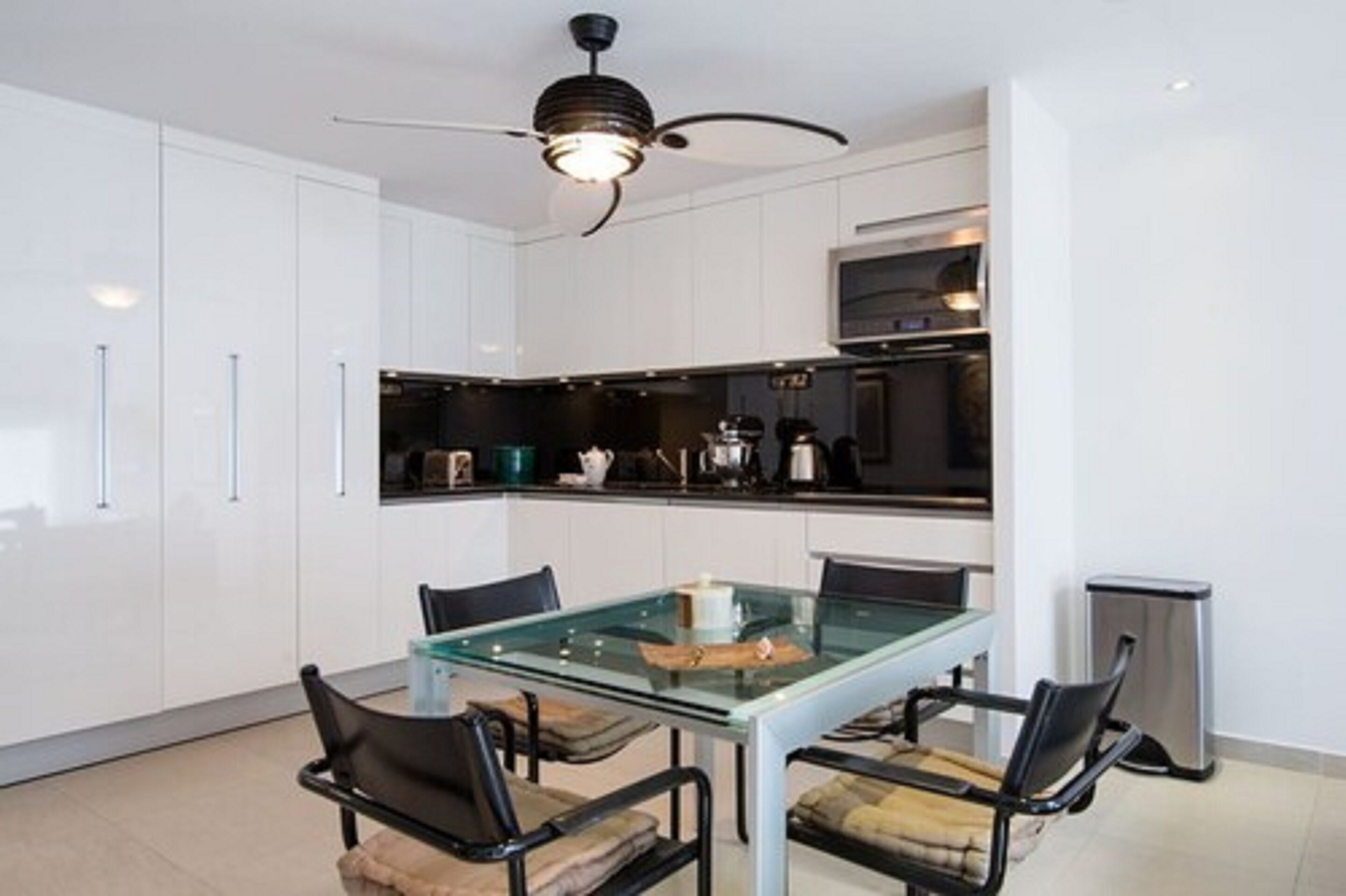 A modern kitchen with white cabinets, a glass dining table, and black chairs.