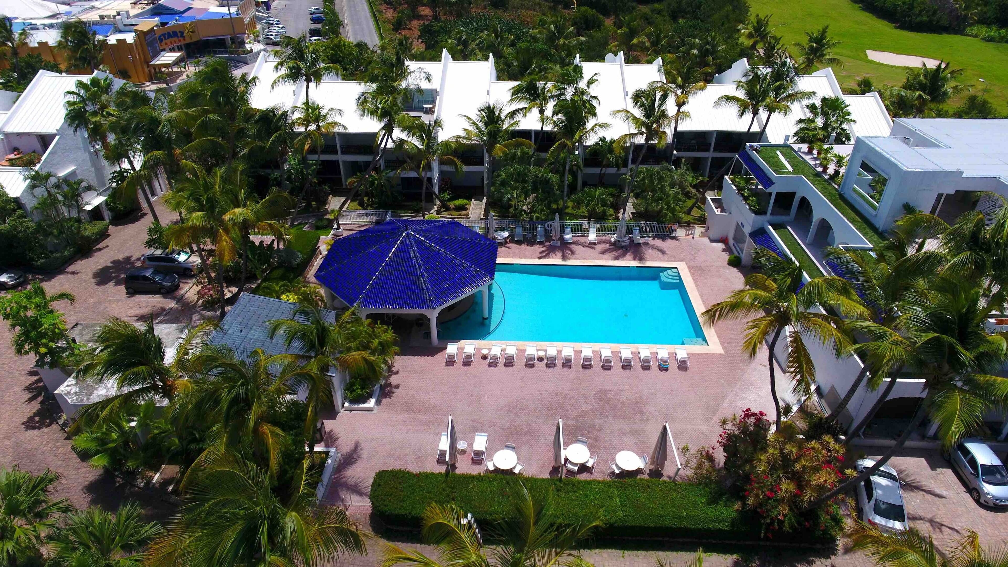 A resort with a central swimming pool, lounge chairs, and palm trees.