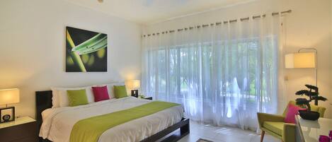 Une chambre à coucher avec un lit, des lampes de chevet, un fauteuil vert, un bureau avec une lampe et un ventilateur de plafond.