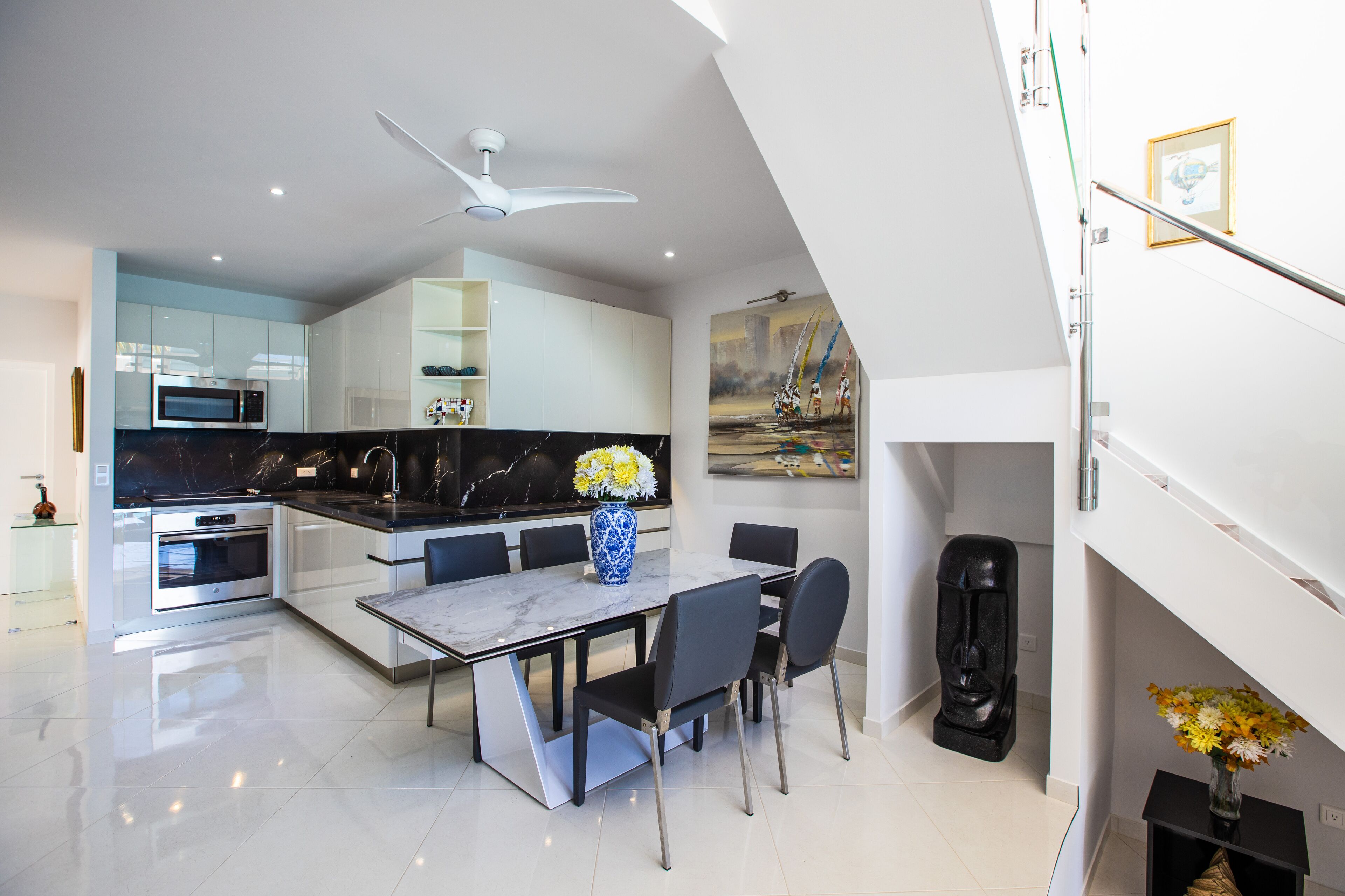 A modern kitchen with a dining area, featuring a marble countertop, a built-in oven, and a ceiling fan.