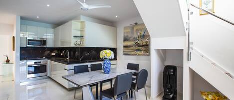 A modern kitchen with a dining area, featuring a marble countertop, a built-in oven, and a ceiling fan.