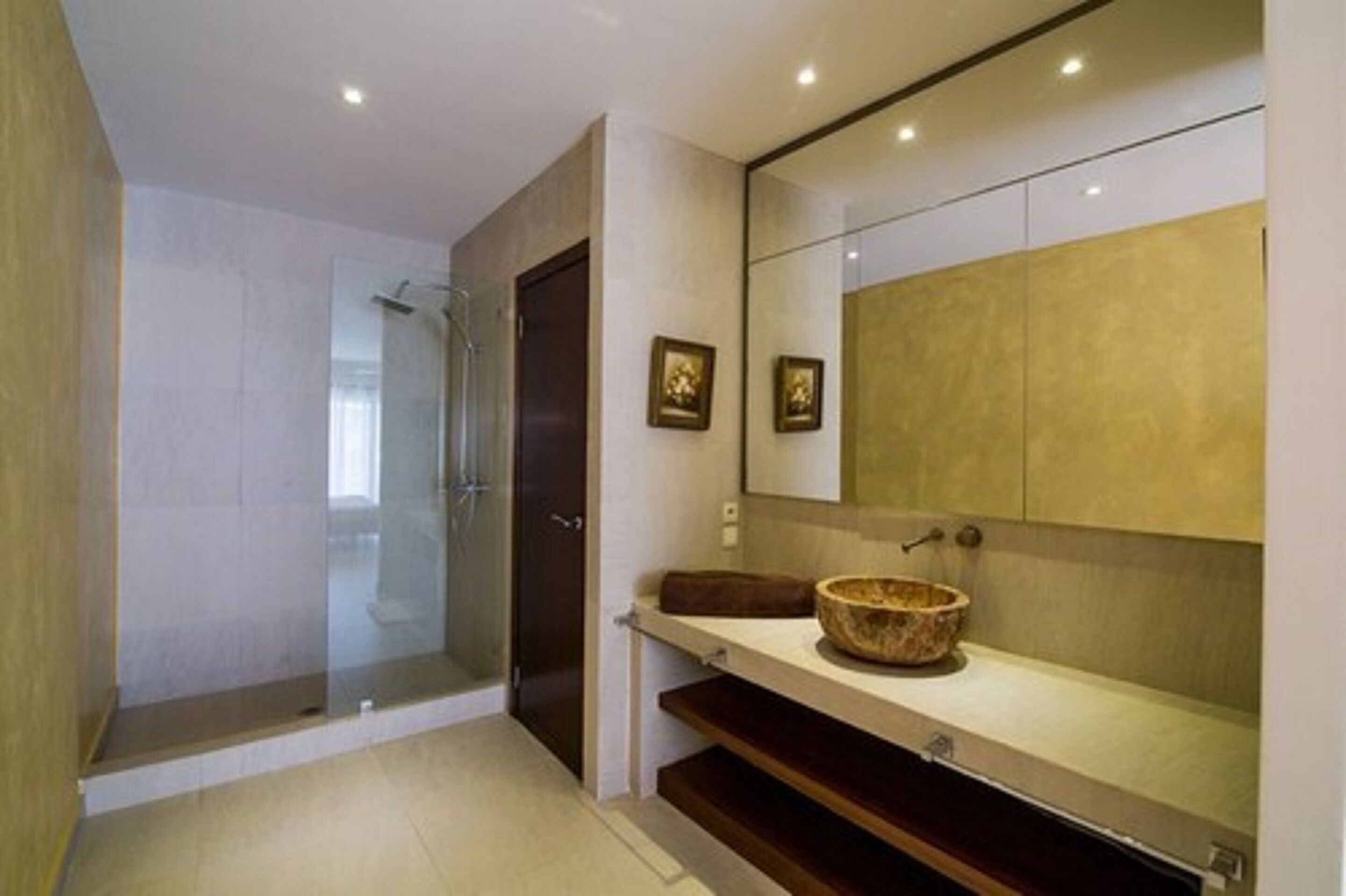 Une salle de bain moderne dotée d’une douche à parois de verre, d’un meuble-lavabo en bois avec un vasque et d’un grand miroir au-dessus du meuble.