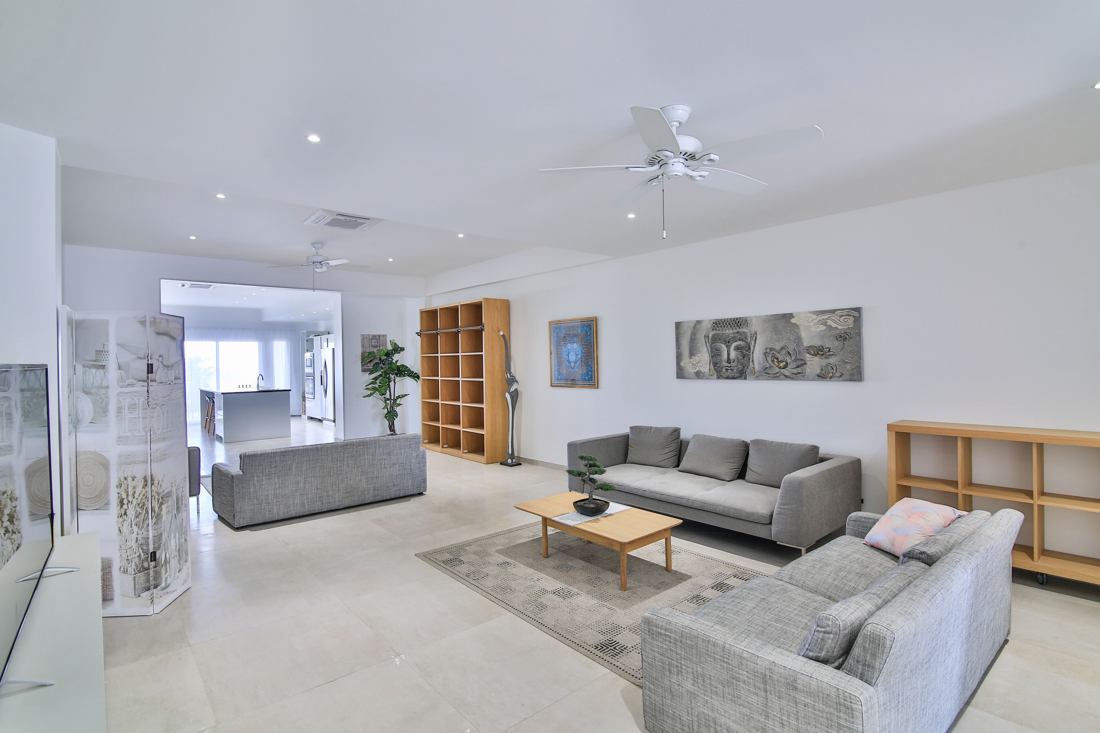 A spacious living room with a grey sofa, a wooden coffee table, and a ceiling fan.