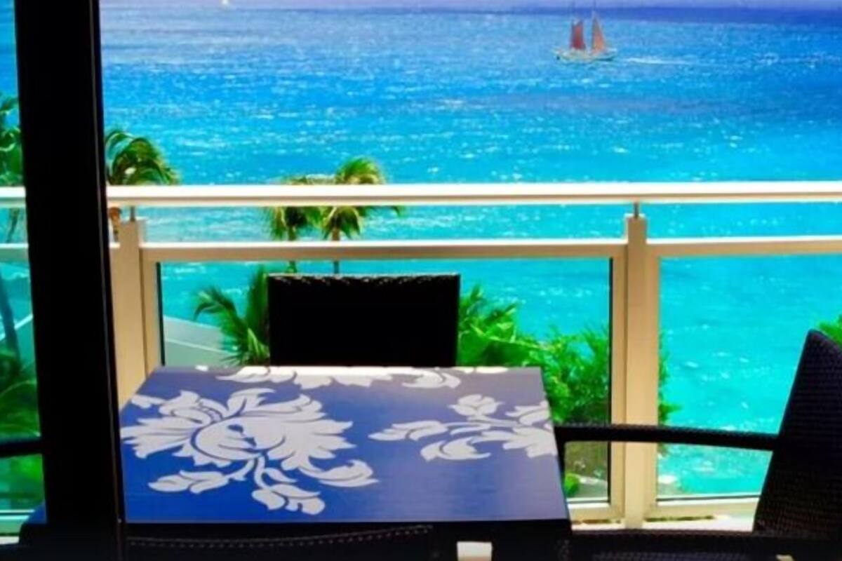 Un balcon avec vue sur l’océan, une table recouverte d’une nappe à motifs floraux et deux chaises.