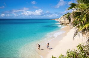 Una playa con aguas turquesas cristalinas, una orilla de arena y un acantilado rocoso con vegetación.