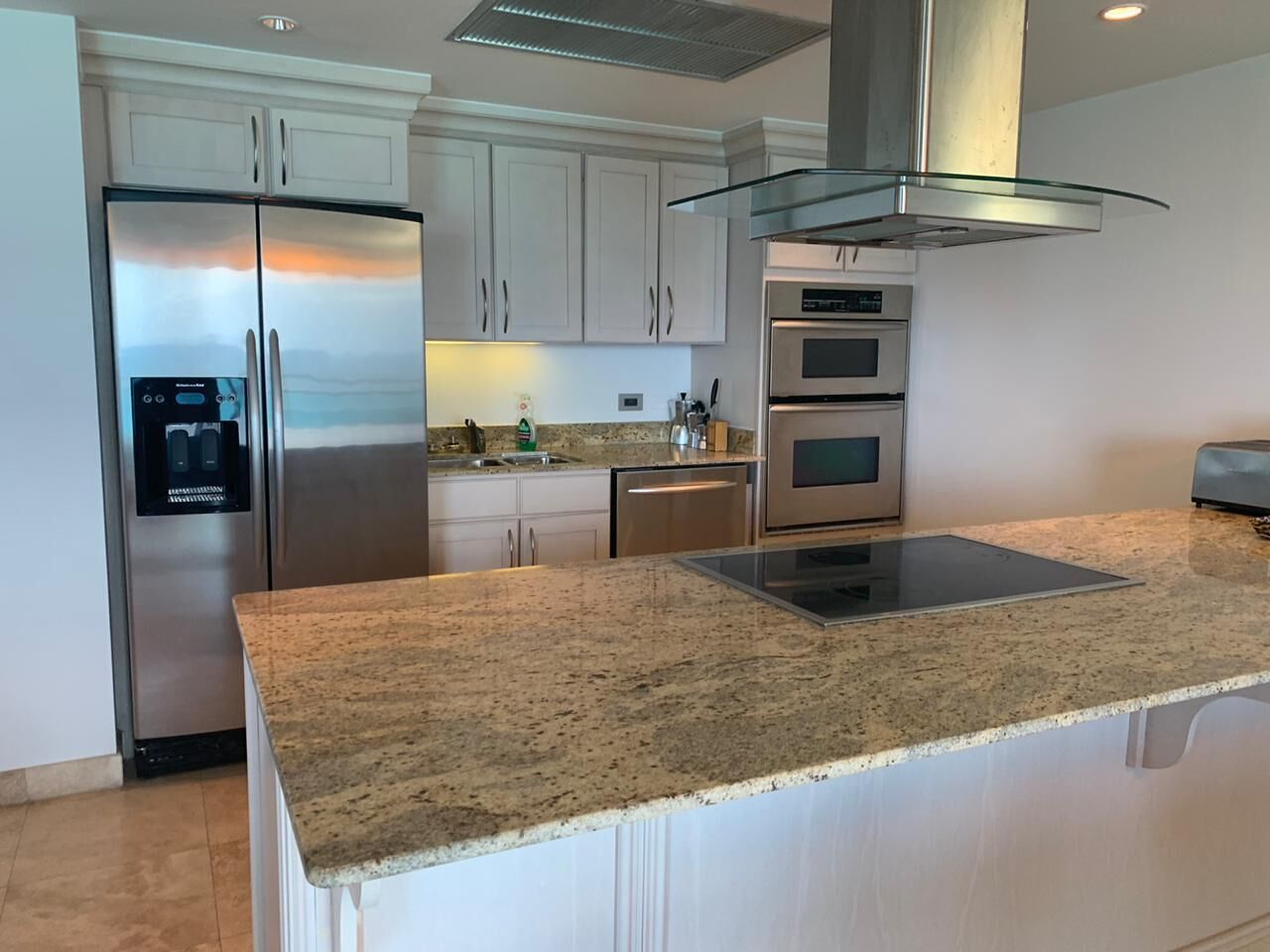 Una cocina moderna con un refrigerador de acero inoxidable, horno empotrado y campana extractora de vidrio.