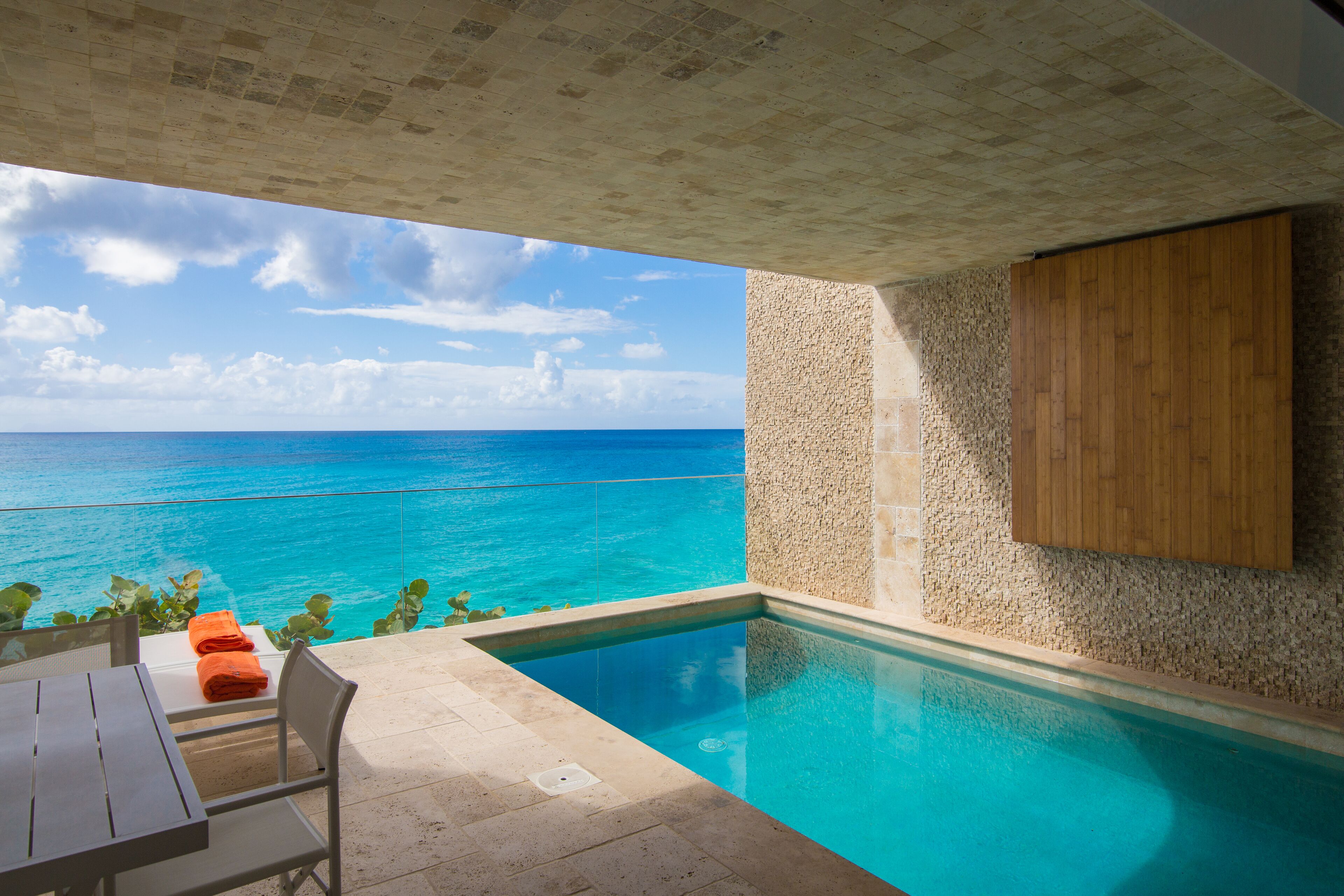 A pool with a view of the ocean, a wooden cabinet, and a table with orange towels.