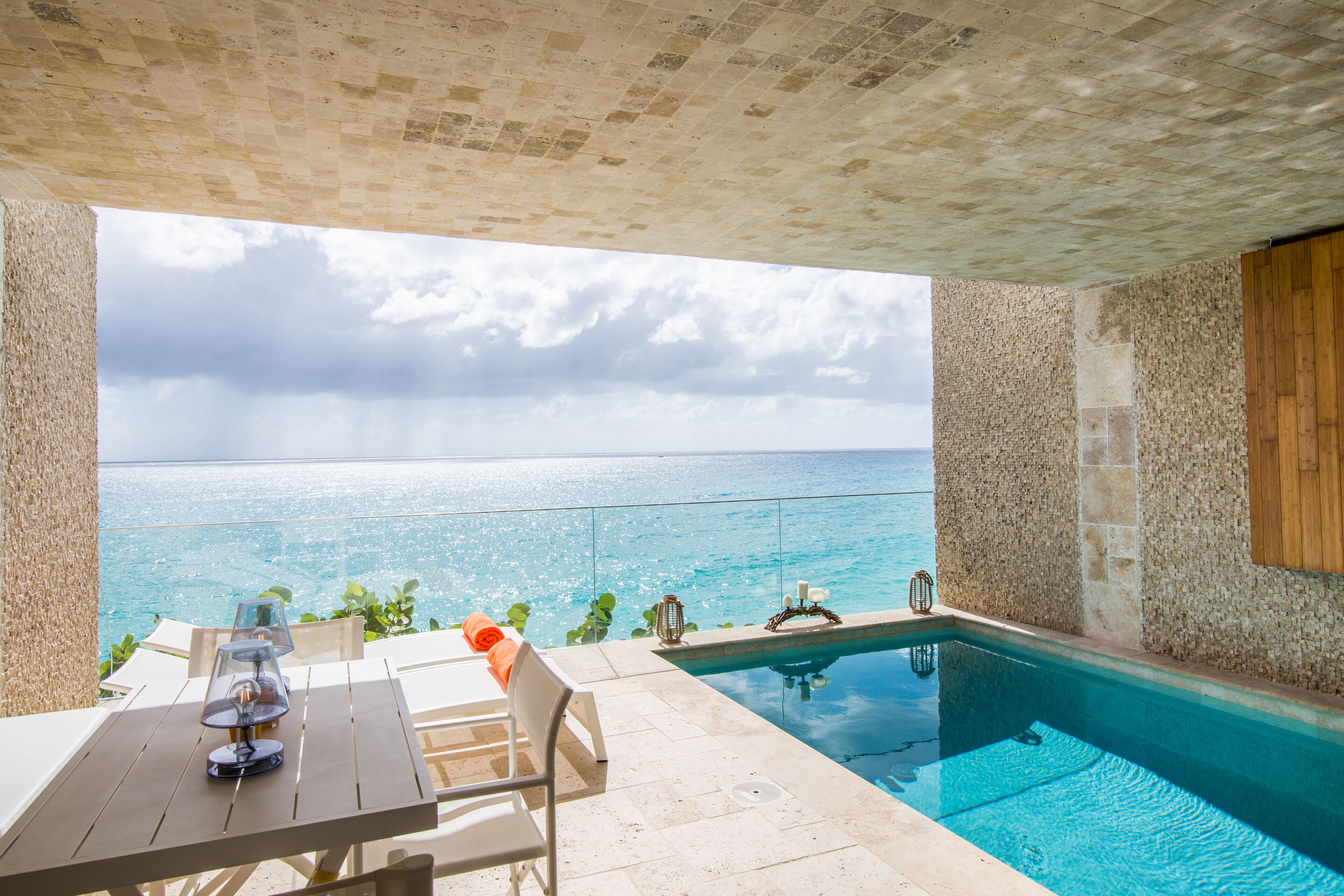 A poolside area with a view of the sea, a table with a lamp, and a chair.
