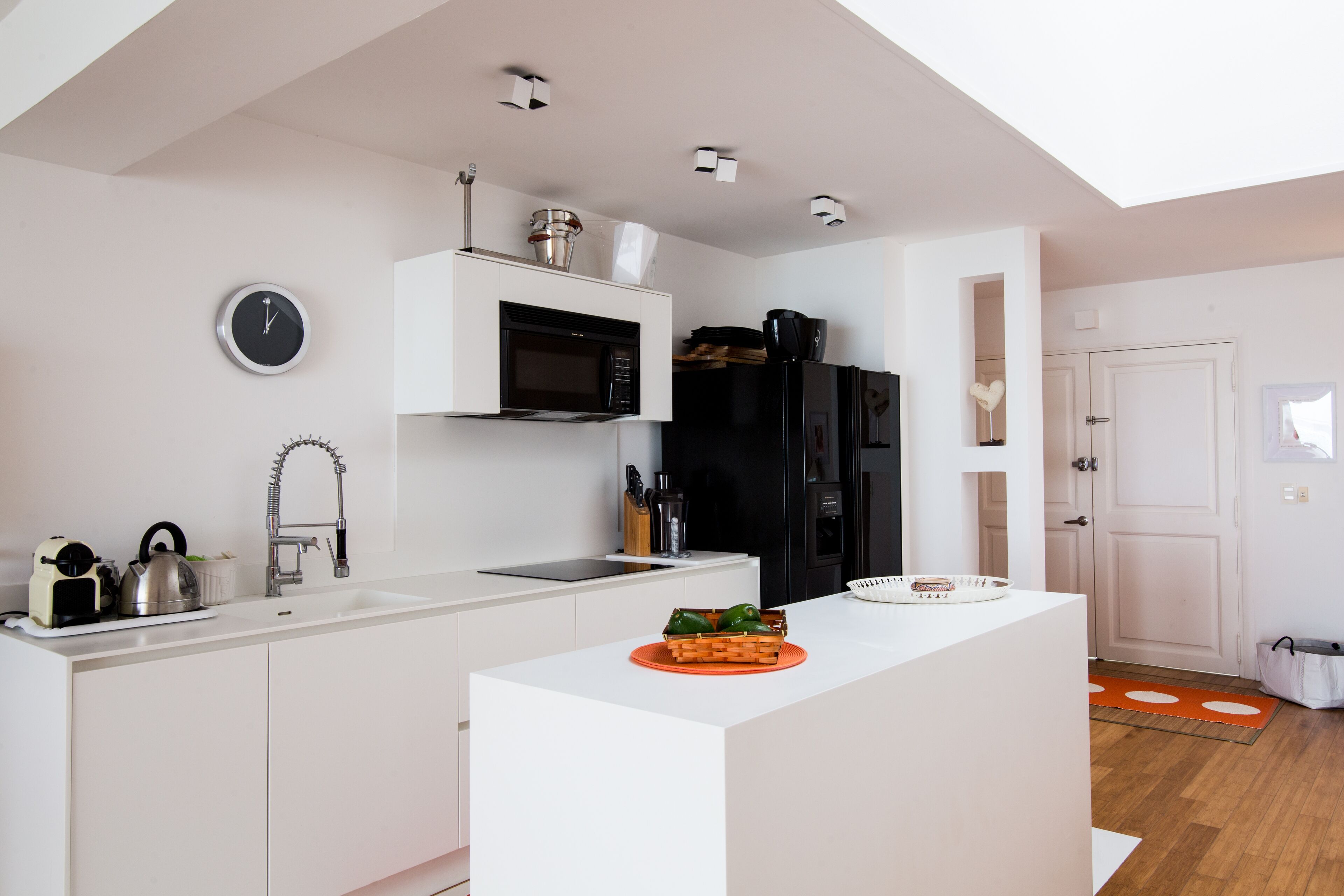 Una cocina moderna con armarios blancos, microondas integrado y un refrigerador negro.
