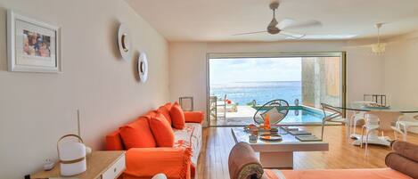 Une chambre moderne avec un plancher en bois, des meubles orange, une table en verre et une vue sur la mer.