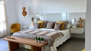 Um quarto moderno com uma cama grande, um banco de madeira, duas cadeiras amarelas e uma mesa de cabeceira com um abajur.