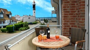 A balcony with a round wooden table, two wicker chairs, a bottle of wine, and a glass of juice. - Apt. Strandschnecke - Dream apartment with partial harbor views! (Insel Poel / OT Timmendorf Strand)