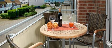 A balcony with a round wooden table, two wicker chairs, a bottle of wine, and a glass of juice.