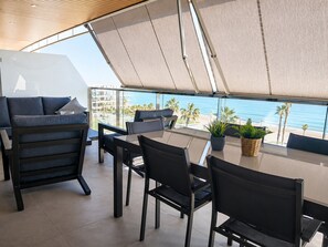 Ein moderner Essbereich im Freien mit Blick auf den Ozean, ausgestattet mit einem Tisch, Stühlen und einem großen Sonnenschirm.