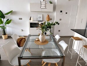 Un espace repas moderne avec une table à plateau en verre, des chaises blanches et une plante en pot.