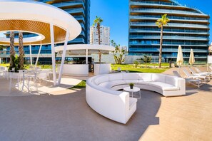 Un espace de détente extérieur moderne, avec des meubles blancs, une disposition des sièges en arc de cercle et une structure circulaire centrale.