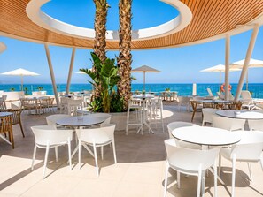 An outdoor seating area with round tables and chairs, palm trees, and a view of the ocean.