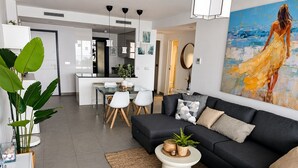 Un salon moderne avec un canapé foncé, une table basse et un coin repas comprenant une table et des chaises en verre.