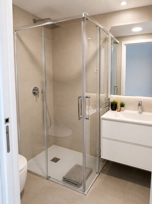 Une salle de bain moderne avec une douche à parois de verre, un lavabo blanc et un miroir au-dessus.