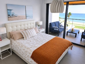 Une chambre à coucher avec un lit, des tables de chevet, une vue sur la plage, un balcon avec une chaise et une table.