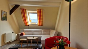 A living room with a sofa, a small table, a red chair, a floor lamp, and a window with curtains.
