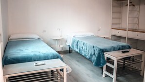 A small, modern room with two single beds, a small table, a sink, and a wardrobe. - Affittacamere Torresi 2 (Ancona)