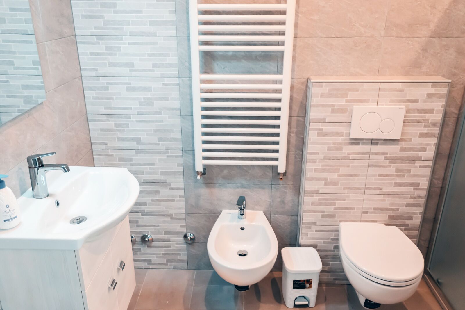 Ein modernes Badezimmer mit einem weißen Waschbecken, Bidet und WC, einem Handtuchhalter und einer Wandheizung.