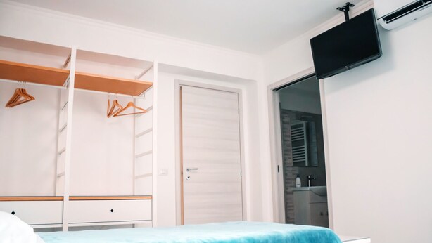 A bedroom with a bed, a wardrobe, a TV, and a bathroom visible through an open door. - Affittacamere Torresi 2 (Ancona)