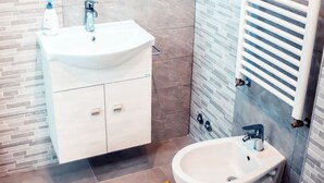 A modern bathroom with a white sink, a bidet, a toilet, and a mirror above the sink. - Affittacamere Torresi 2 (Ancona)