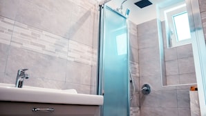 A modern bathroom with a glass shower enclosure, a sink with a chrome faucet, and a tiled wall with a brick pattern. - Affittacamere Torresi 2 (Ancona)