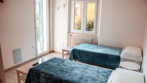 A small, bright room with two beds, a window, and a radiator. - Affittacamere Torresi 2 (Ancona)