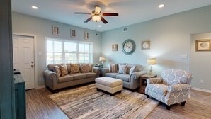 A living room with a ceiling fan, two sofas, a patterned armchair, and a rug.