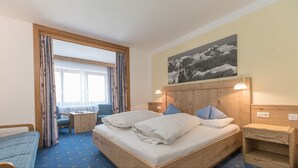 A hotel room with a large bed, a desk, a chair, and a view of the outdoors through a large window. - Pension Trojerhof (Heiligenblut)