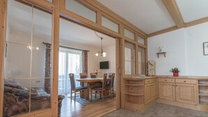 A spacious room with a large dining table, wooden cabinets, and a cozy seating area with a sofa. - Pension Trojerhof (Heiligenblut)
