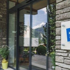 Ein Gebäudeeingang mit Glastür, Steinwand und einem Schild mit blauem Hintergrund.