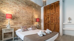 A bedroom with a large bed, two bedside tables, a brick wall, wooden wardrobe, and a small shelf with a decorative item. - MY LOFT 4 YOU RUZAFA STYLE III (Valencia)