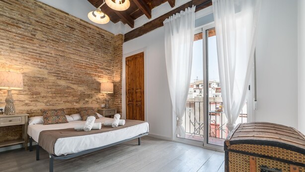 A bedroom with a wooden wall, a bed with white linens, a wooden chest, and a balcony with a view of buildings. - MY LOFT 4 YOU RUZAFA STYLE III (Valencia)