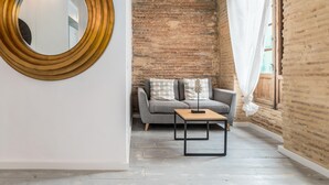A modern living room with a brick wall, a round mirror, a grey sofa, and a small wooden table. - MY LOFT 4 YOU RUZAFA STYLE III (Valencia)