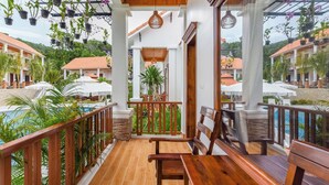 Un balcon abrité avec des balustrades en bois, un banc en bois et des orchidées en pot suspendues.
