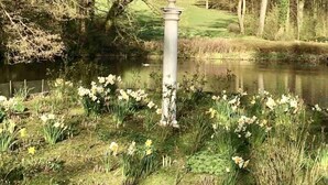 A serene garden with a classical column, a pond, and daffodils. - Exklusives Wohnen am Stadtpark (Bad Driburg)