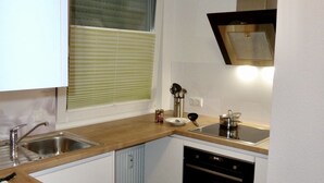 A compact kitchen with a dishwasher, a stove, and a window with blinds. - Exklusives Wohnen am Stadtpark (Bad Driburg)