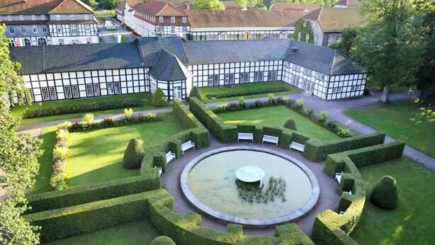 A large, traditional building with a symmetrical garden layout, including a central circular lawn and surrounding hedges. - Exklusives Wohnen am Stadtpark (Bad Driburg)