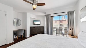 Hotelkamer met een groot bed, een bureau, een stoel, een televisie, een kledingkast en een balkon met uitzicht op gebouwen.